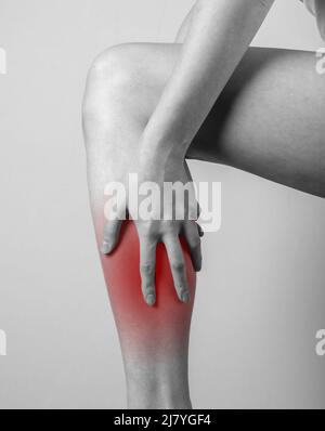 Douleur de shin. Femme tenant une jambe avec un point rouge. Tendons, inflammation des muscles, blessures, conséquences des ecchymoses osseuses. Noir et blanc. Photo de haute qualité Banque D'Images