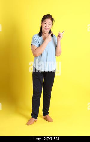 La femme asiatique âgée porte une chemise bleu clair sur fond jaune. Banque D'Images