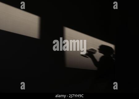 Ombre sur le mur d'un sommelier féminin avec un verre de vin. Chiaroscuro de la fenêtre. Copier l'espace. Banque D'Images