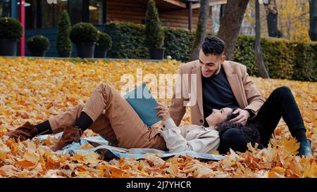 Heureux couple dans l'amour avec enthousiasme lire le livre dans le parc d'automne jeune homme espagnol et femme hispanique attrayante riant belle fille se trouve sur Banque D'Images