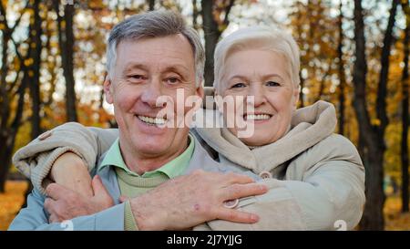 La vieille femme adulte enterre mari aimé par les épaules couple marié âgé embrassant dans le parc d'automne grands-parents souriant regardant la caméra puis l'un l'autre Banque D'Images