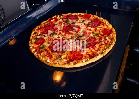 femme ouvrir des fours et prendre des pizzas avec des tomates, des olives, des champignons et des saucisses au fromage Banque D'Images