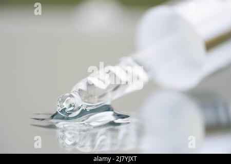 Compte-gouttes en verre avec liquide transparent sur fond en verre avec espace de copie. Texture du sérum facial ou de l'huile cosmétique. Mise au point sélective, photo macro Banque D'Images