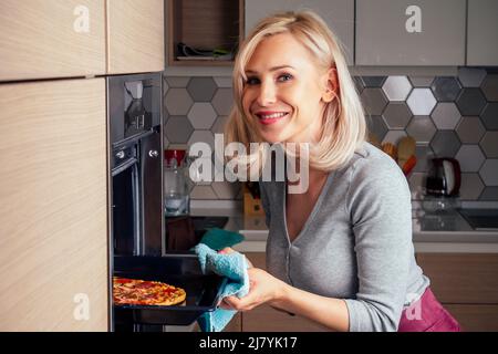 femme ouvrir des fours et prendre des pizzas avec des tomates, des olives, des champignons et des saucisses au fromage Banque D'Images