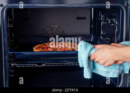 femme ouvrir des fours et prendre des pizzas avec des tomates, des olives, des champignons et des saucisses au fromage Banque D'Images