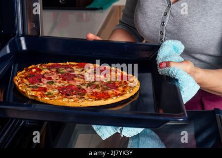 femme ouvrir des fours et prendre des pizzas avec des tomates, des olives, des champignons et des saucisses au fromage Banque D'Images