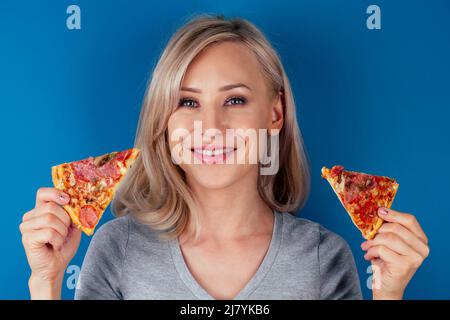 femme ouvrir des fours et couper de la pizza avec des tomates, des olives, des champignons et des saucisses de fromage sur fond bleu dans le studio Banque D'Images