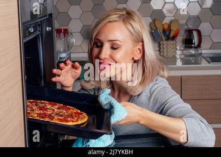 femme ouvrir des fours et prendre des pizzas avec des tomates, des olives, des champignons et des saucisses au fromage Banque D'Images