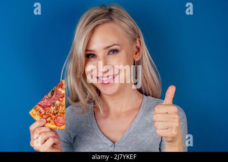 femme ouvrir des fours et couper de la pizza avec des tomates, des olives, des champignons et des saucisses de fromage sur fond bleu dans le studio Banque D'Images