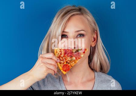 femme ouvrir des fours et couper de la pizza avec des tomates, des olives, des champignons et des saucisses de fromage sur fond bleu dans le studio Banque D'Images