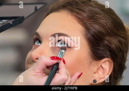 La styliste maîtresse fait le maquillage pour les yeux d'une fille dans un salon de beauté. Banque D'Images