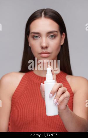 Portrait d'une belle jeune femme en haut orange pulvérisant vos mains avec un antiseptique pendant une pandémie de coronavirus Banque D'Images