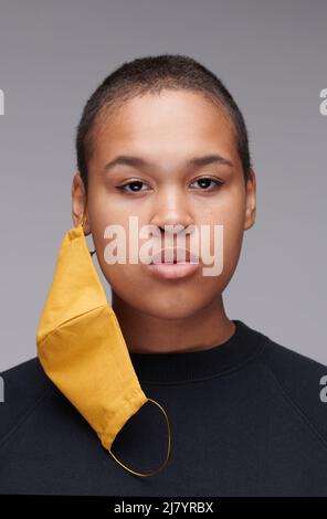 Portrait d'une jeune femme afro-américaine sérieuse avec buzz coupé en utilisant le masque facial jaune pour la protection, concept de coronavirus Banque D'Images