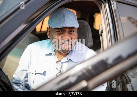 portrait d'un homme africain assis dans sa voiture, souriant, portant une casquette plate Banque D'Images