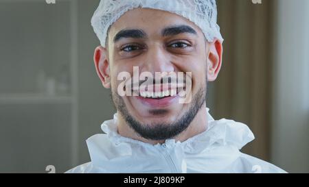 Sourire médecin arabe chirurgien hispanique infirmier travailleur médical en uniforme spécial chapeau regarde la caméra sourire en dents de souris après un travail réussi Banque D'Images