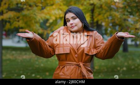 Une jeune femme hispanique troublante debout à l'extérieur dans le parc hausser les épaules douteux regardant la caméra incertain ne sait pas quoi répondre Banque D'Images