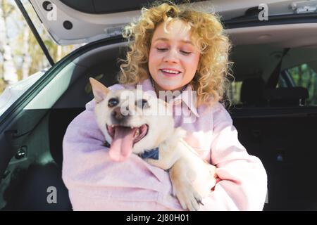 Charmante blonde européenne fille embrassant son chien mignon tout en étant assis dans le coffre de voiture moyen coup animaux de l'extérieur et les humains concept. Photo de haute qualité Banque D'Images