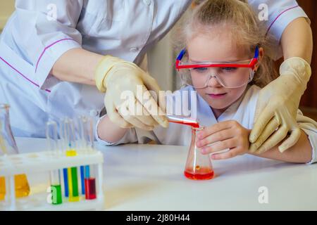 intelligent blonde école fille chimiste dans les lunettes et blanc robe médicale faisant des expériences de la science chimie, mélange de différentes solutions chimiques dans Banque D'Images