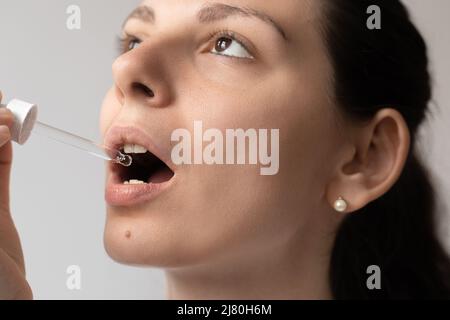 Portrait de la jeune femme aux cheveux foncés prenant un supplément d'huile avec un compte-gouttes en verre. CBD huile de médecine de chanvre appliquée sur la langue Banque D'Images