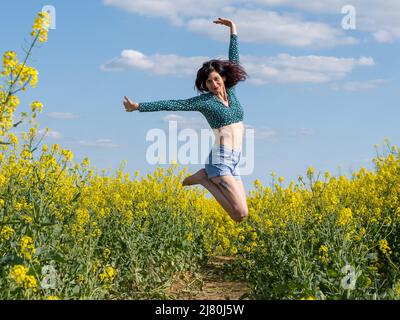 Femme souriante sautant dans un champ de colza au printemps, en France Banque D'Images