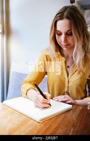 portrait vertical d'une jolie femme blonde écrivant à la main sur un carnet Banque D'Images