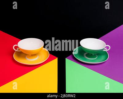 Deux tasses de thé vides colorées qui se levent des soucoupes sur deux tables multicolores Banque D'Images