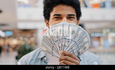 Heureux riches homme d'affaires afro-américain souriant, regardant la caméra portant un fan d'argent se cachant derrière des billets en dollars montrant des billets financiers Banque D'Images
