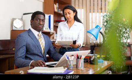 Homme d'affaires afro-américain concentré assis sur le lieu de travail avec une collègue féminine Banque D'Images