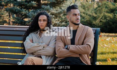 Couple sullen assis sur le banc dans le parc homme et la femme s'assoient avec les bras croisés amants querelle ignorant les uns les autres arabe en colère gars et mauriquement offensé fille Banque D'Images