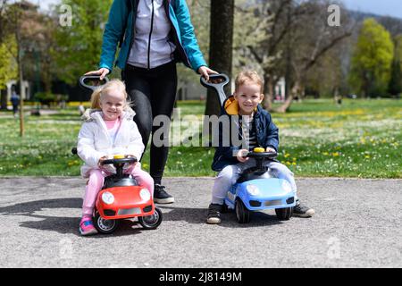 Les parents et les enfants jouent avec une voiture miniature en plein air dans le parc - Un joyeux garçon et une fille se promette dans une voiture miniature bleue et rouge dans la rue Banque D'Images