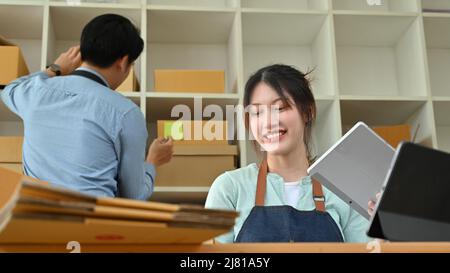 Startup PME entrepreneur d'affaires, Femme travaillant sur tablette, la vérification des commandes en ligne et un homme vérifiant le stock de produits sur les étagères. Couple faire un b Banque D'Images