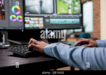 Gros plan d'un éditeur vidéo numérique installé sur un bureau à plusieurs moniteurs tout en travaillant sur des films. Vidéaste créatif de la maison de post-production améliorant la qualité visuelle des cadres de film. Banque D'Images