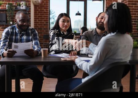 Les recruteurs de la société de marketing sont assis à la réception au bureau tout en accueillant le candidat à l'entrevue d'emploi. Femme afro-américaine qui secoue le chef de l'équipe de recrutement tout en faisant bonne première impression. Banque D'Images