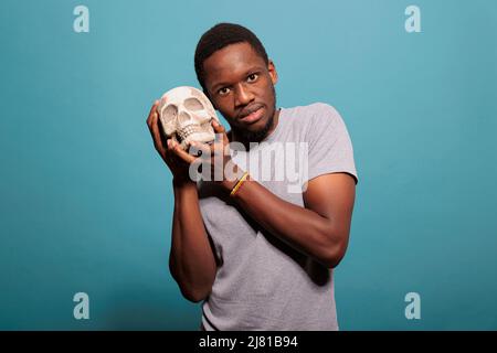 Homme décontracté montrant les os du crâne humain devant la caméra, étudiant la médecine scientifique pour apprendre la connaissance du squelette. Jeune adulte tenant un sujet anatomique pour la leçon de biologie et d'anatomie. Banque D'Images