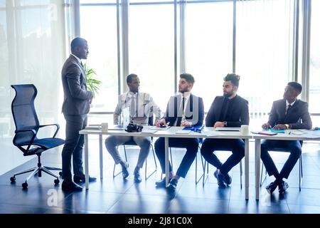 patron afro hommes d'affaires parlant avec un collègue de partenaires arabes, équipe multiethnique dans le bureau avec fenêtre panoramique. Banque D'Images