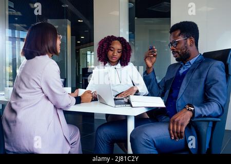 une équipe créative composée d'hommes multiraciaux assis autour du bureau dans des vêtements formels parlant du nouveau projet dans la salle de réunion Banque D'Images