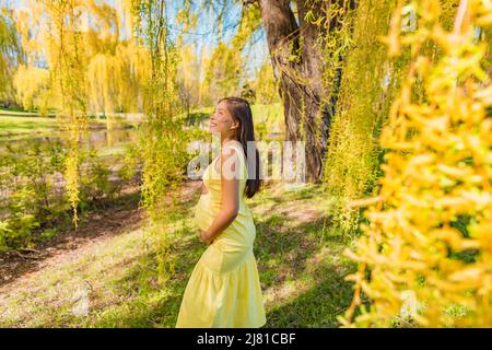 Grossesse maternité jeune asiatique s'attendre à ce que la femme marche dans les saules jaunes parc arbres heureux de détente en plein air dans la nature. Style de vie printanier, en bonne santé Banque D'Images