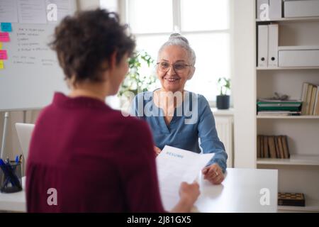 Femme recruteuse senior souriant au jeune candidat pendant l'entrevue d'emploi. Banque D'Images