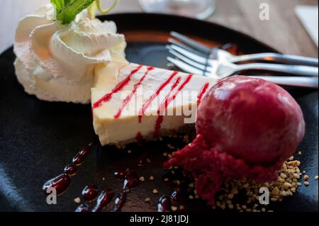 Morceau de cheesecake à la ricotta servi avec de la glace cassis, de la crème fouettée et de la menthe fraîche, desserts sucrés Banque D'Images