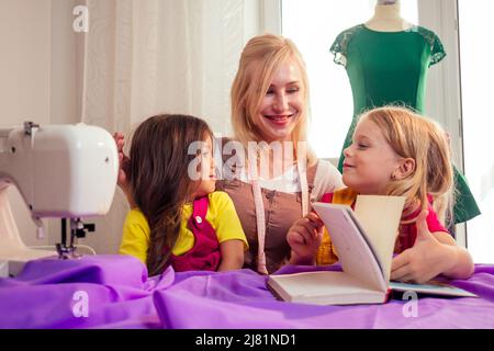 Souriante et heureuse, la mère blonde en multitâche enseigne à une petite sœur à coudre par elle-même sur une machine à coudre Banque D'Images