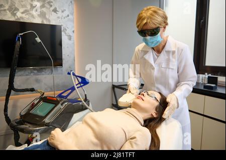 Esthéticienne effectuant un rajeunissement au laser dans un salon de beauté. Procédure d'épilation Elos sur le visage d'une femme. Esthéticienne faisant le laser rajeunati Banque D'Images