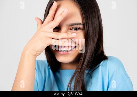 Honte et drôle jeune fille avec des bretelles couvrant le visage avec la main. Isolé sur blanc Banque D'Images