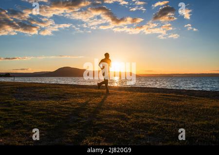 Image de silhouette d'un homme qui court au bord du lac Rotorua au coucher du soleil, Rotorua, Nouvelle-Zélande. Banque D'Images