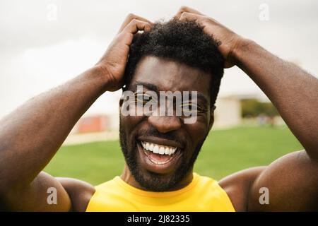 Homme transgenre africain avec maquillage souriant sur l'appareil photo extérieur - Focus sur le visage Banque D'Images