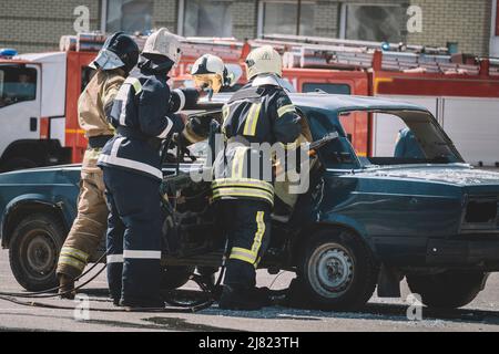 Pompier avec salopette de protection et gants de travail tout en brisant le pare-brise d'une voiture. Premiers soins après un accident sur la route. Banque D'Images