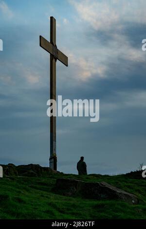 Figure solitaire au sommet d'une colline, grande croix de Pâques en bois (commémorant la crucifixion) et ciel ensoleillé - le Chevin, Otley, West Yorkshire England UK. Banque D'Images