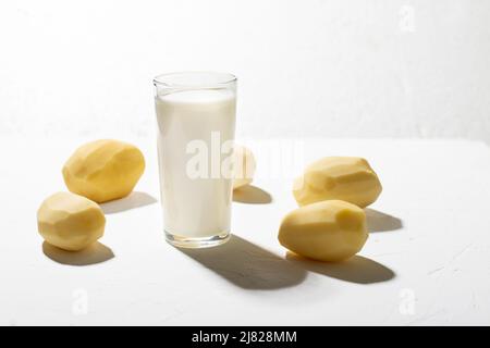 Alternative au lait de pomme de terre.Un verre de lait et une pomme de terre crue sur fond blanc. Banque D'Images