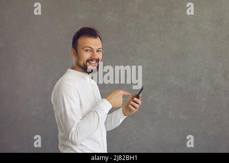 Un jeune homme heureux utilisant un téléphone portable isolé sur fond gris de l'espace de copie Banque D'Images