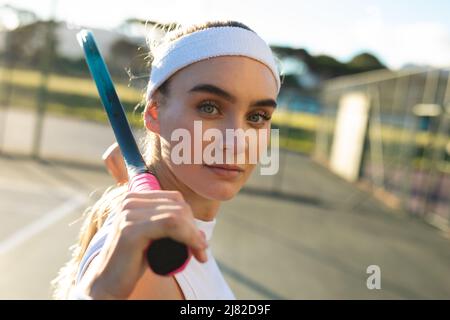 Vue latérale portrait d'une jeune femme de tennis caucasienne très confiante debout avec une raquette Banque D'Images
