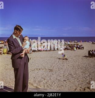 Un père tient un bébé sur la plage de Corton, Suffolk, en 1957. Cette image a été prise à partir de la diapositive d'origine. Banque D'Images